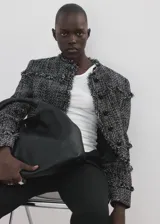 Chaqueta de tweed en tejido jaspeado negro y blanco, con diseño recto, cuello redondo, manga larga y cierre delantero con botones. Presenta terminaciones deshilachadas y detalles de flecos.