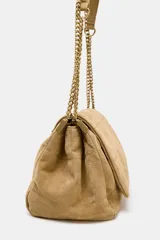 Bolso de hombro confeccionado en piel de ante color tostado, con diseño acolchado mediante pespuntes horizontales y verticales. Cuenta con una correa de cadena metálica dorada con refuerzo de piel y cierre mediante solapa con imán.