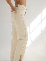 Pantalon de gabardina color beige, de corte recto y tiro medio. Presenta alforzas verticales en los laterales que recorren el largo de la pierna y cierre frontal con botón.