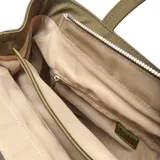 Cartera tipo tote de tela color verde oliva, con doble asa de hombro y detalle de borla decorativa con cordones en uno de los laterales. Incluye un aplique circular metálico con el logo de la marca en la parte frontal.
