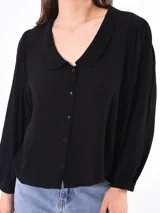 Camisa negra de manga larga con cuello redondo y cierre frontal de botones. La tela parece tener textura y las mangas son abullonadas con puños ajustados.