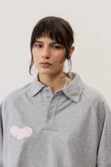 Buzo celeste de manga larga con cuello polo y cierre frontal de botones. Presenta un parche marrón bordado en el pecho.