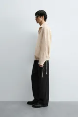 Camisa de manga larga color beige claro con textura jacquard arrugada, cuello solapa con abertura en V y bolsillo canguro frontal. Posee cordones ajustables en el bajo lateral.