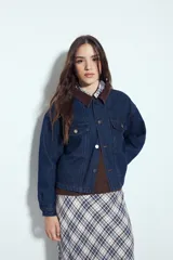 Campera de jean color negro con cuello de pana en tono marrón, cierre frontal con botones y bolsillos en el pecho. Presenta un diseño de corte relajado y ligeramente cropped, con interior forrado en corderito para mayor abrigo.