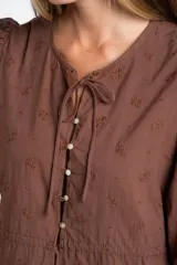 Blusa negra de algodón con diseño de broderie, mangas tres cuartos abullonadas, cierre frontal con botones y detalle de cordón ajustable en la cintura.