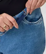 Pantalón mom jeans de tiro alto y corte holgado en caderas y piernas, con bolsillos, presillas para cinturón y cierre frontal con botón.