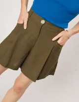 Short color beige de lino con tiro alto, elástico en la pretina trasera, cierre delantero con botón, tablas en el frente, bolsillos delanteros y dobladillo invisible.