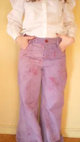 Pantalón de gabardina tiro alto y pierna amplia, teñido a mano con tintes naturales en color violeta con efecto de chispas y salpicaduras. Cuenta con bolsillos delanteros y traseros, presillas para cinto y recortes decorativos en las piernas.