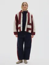 Campera de sherpa con diseño de rayas verticales en color bordó y crema. Presenta cuello alto, cierre frontal con broches a presión, mangas largas y bolsillos frontales aplicados con vivos a contratono.