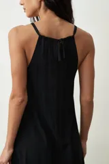 Vestido midi de color negro con escote halter y breteles finos. Presenta un corte holgado y fluido con caída suave.