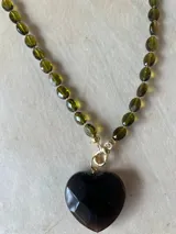 Collar con dije de corazón facetado en color verde esmeralda, con cadena de cuentas de cristal facetadas en tonos amarillos y dorados.