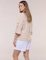 Blusa Erika de algodón con estampado de rayas en tonos azules, rosados y amarillos. Presenta cuello redondo con escote en V y botones frontales, mangas cortas decoradas con una fila de botones en los laterales y dobladillo asimétrico.