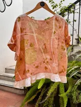 Top de lino con estampado botánico artesanal (ecoprint) en tonos rosados y ocres. Presenta mangas cortas con volados y un volado decorativo en el ruedo inferior en color blanco.