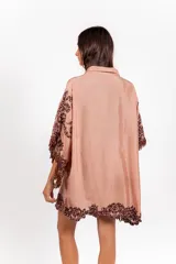 Vestido corto de silueta amplia, color tostado con bordados barrocos en contraste, escote en V con botones de madera, mangas anchas tipo capa con flecos de cuentas en los bordes.