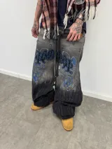 Jean de corte amplio en color negro con efecto acid wash. Presenta cierres laterales metálicos que permiten ajustar la silueta entre corte recto, oxford o baggy. Incluye una estampa gráfica de gran tamaño en la parte trasera con detalles bordados, bolsillos amplios y una etiqueta de cuero legítimo en la cintura.