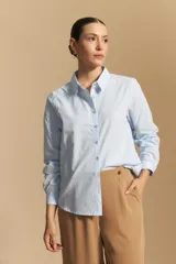 Camisa de corte clásico y holgado, confeccionada en tela blanca, con cuello camisero, cierre frontal de botones de nácar y mangas largas con puños abotonados.