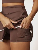 Falda skort deportiva color chocolate con short integrado, confeccionada en tejido técnico de secado rápido con borde inferior en contraste blanco.