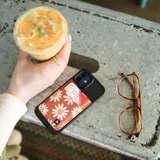 Billetera porta tarjetas Thread con diseño de margaritas blancas sobre fondo marrón y solapa superior de cuero marrón.