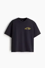 Remera negra de algodón con corte boxy y oversized, cuello redondo y mangas cortas. Cuenta con un pequeño estampado dorado en el pecho con texto y estrellas.