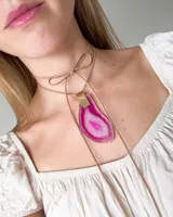 Collar con dije de piedra ágata rosa y blanca, con engarce dorado y cordón de cuero sintético color beige que se ata al cuello.