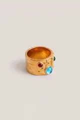 Anillo ancho de metal dorado con acabado texturizado irregular, decorado con piedras incrustadas de colores rojo, azul y verde.