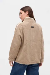 Campera de sherpa color marrón con diseño capitoneado, cierre frontal completo y detalles en color blanco. Presenta cuello alto, bolsillos laterales y puños elásticos.
