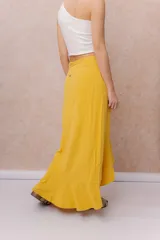 Falda larga envolvente de color mostaza, con diseño asimétrico, lazo ajustable en la cintura y volados en cascada.