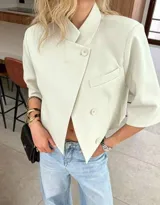 Chaqueta cropped de diseño estructurado en color crema, con cuello alto, cierre frontal cruzado con botones y mangas 3/4. Presenta un bolsillo decorativo en el frente y un corte asimétrico.