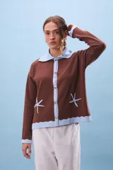 Cárdigan de tejido punto color marrón con cuello y ribetes en celeste claro. Presenta bordados de estrellas de mar en color celeste en la parte delantera inferior.