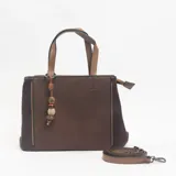 Cartera tipo tote de diseño estructurado en color marrón, combinando paneles de textura lisa y granulada. Incluye doble asa superior, correa larga ajustable y extraíble, y un colgante decorativo con cuentas de piedra en el asa.
