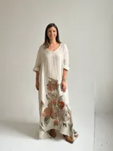 Vestido largo beige con diseño holgado, escote en V y mangas largas, adornado con un gran estampado floral en tonos marrones y verdes en la parte inferior.