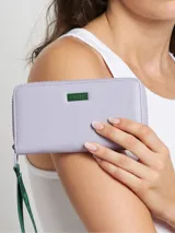 Billetera grande de poliuretano color lila con cierre perimetral y logo rectangular metálico en el frente. Incluye correa de mano verde con estampado.