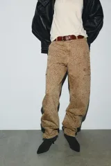 Jeans tiro medio, corte baggy balloon, color marrón claro con estampado animal moteado en tono más oscuro. Presenta bolsillos laterales, bolsillos cargo con solapa en las piernas y bolsillos de plastrón en la espalda. El bajo es ajustable con botón a presión.