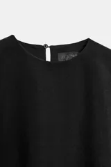 Vestido corto negro de cuello redondo y manga sisa, con detalle de capa asimétrica superpuesta y cierre posterior con botón.