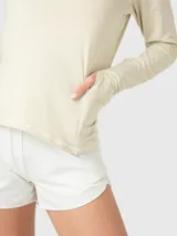 Remera deportiva de manga larga en color beige, confeccionada en tela reciclada suave. Presenta un diseño con cuello alto y medio cierre frontal, además de un bolsillo lateral integrado. Las mangas incluyen aberturas para los pulgares.