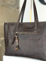 Bolso tipo shopper de cuero marrón chocolate, con doble asa de hombro, cierre superior y bolsillo frontal con cierre y tirador decorativo de cuero con estampa animal print.