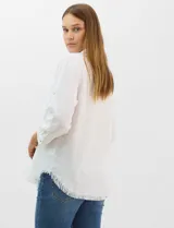 Camisa de tencel color blanco, con cuello camisero, cierre frontal de botones y dos bolsillos en el pecho. Presenta mangas largas con presilla para regular el largo y ruedo con detalle de flecos.