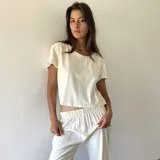 Conjunto de dos piezas compuesto por una remera de corte recto y cuello redondo, y un pantalón de tiro medio con cintura elástica. Ambas prendas están confeccionadas en lino de color manteca.