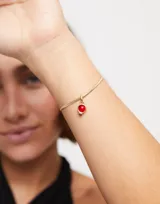 Dije charm con forma de globo, bañado en oro de 18k y con piedra roja.