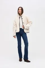 Campera de sherpa doble faz en color crema, con cierre frontal de botones y detalles de vivos en nylon negro. Presenta bolsillos laterales con ribetes en contraste y cuello alto.