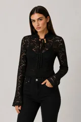 Top de encaje negro con mangas largas acampanadas, cuello mao con cierre de lazo frontal y diseño ajustado al cuerpo.