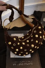 Bolso pequeño de hombro con forma de media luna, color negro, decorado con tachas redondas doradas. Cuenta con una correa ajustable y herrajes dorados.