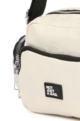 Bandolera de diseño funcional en color blanco, con múltiples compartimentos con cierre, bolsillos laterales y correa ajustable. Incluye una etiqueta frontal con la frase 'Not just a bag'.
