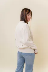 Sweater de tejido fino color beige, con cuello redondo, mangas largas y terminaciones acanaladas. Presenta un diseño con detalles trenzados en diagonal en el frente y corte relajado.