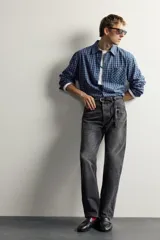 Jeans straight fit de corte recto y tiro medio, confeccionados en denim de algodón rígido con efecto lavado en color negro, de la colección especial Aaron Levine x Zara. Presentan diseño clásico de cinco bolsillos y cierre frontal con botonadura.
