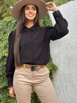 Camisa de manga larga color negro, con cuello alto y cierre frontal de botones. Presenta detalles de encaje y bordados verticales a lo largo de toda la prenda, incluyendo los puños.