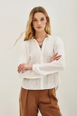 Camisa de algodón y viscosa color blanco, con mangas largas y diseño frontal con bordados geométricos y florales en contraste negro. Presenta cuello redondo con pequeña abertura y cierre frontal de botones.