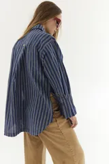 Camisa azul a rayas verticales con cuello clásico, manga larga con puños abotonados y corte holgado.