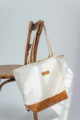Bolso tipo tote de lona color crudo con base y asas de cuero color marrón.