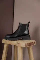 Botas tipo Chelsea de cuero con acabado vintage, diseño de caña media con paneles elásticos laterales y suela track robusta.